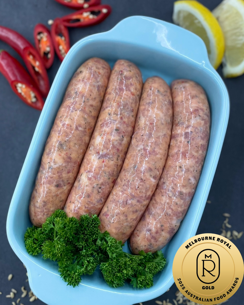 Four raw sausages in a blue container with parsley, red chili peppers, and lemons on a dark surface. Gold medal Gourmet Sausage Category 2025 Melbourne Royal Australian Food Awards
