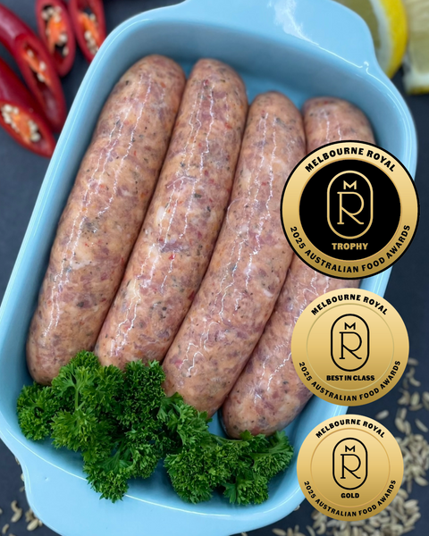 Four of The Lucky Pig’s Leaning Tower Italian-style sausages in a blue tray, garnished with fresh parsley, with Melbourne Royal 2025 Champion Trophy, Best in Class, and Gold medal badges displayed.